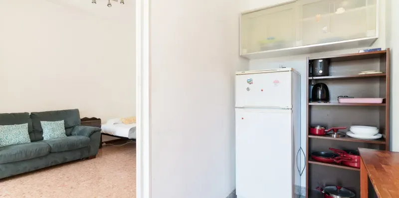A living area and kitchenette with a refrigerator, open shelving, and seating.