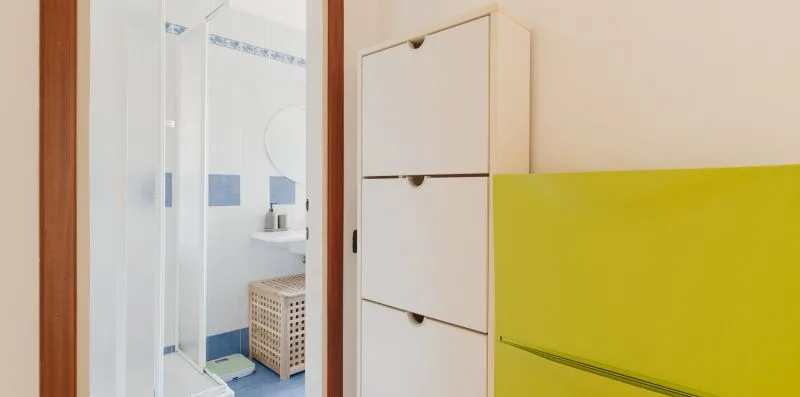 A bathroom with a glass shower beside white cabinets and a yellow panel.