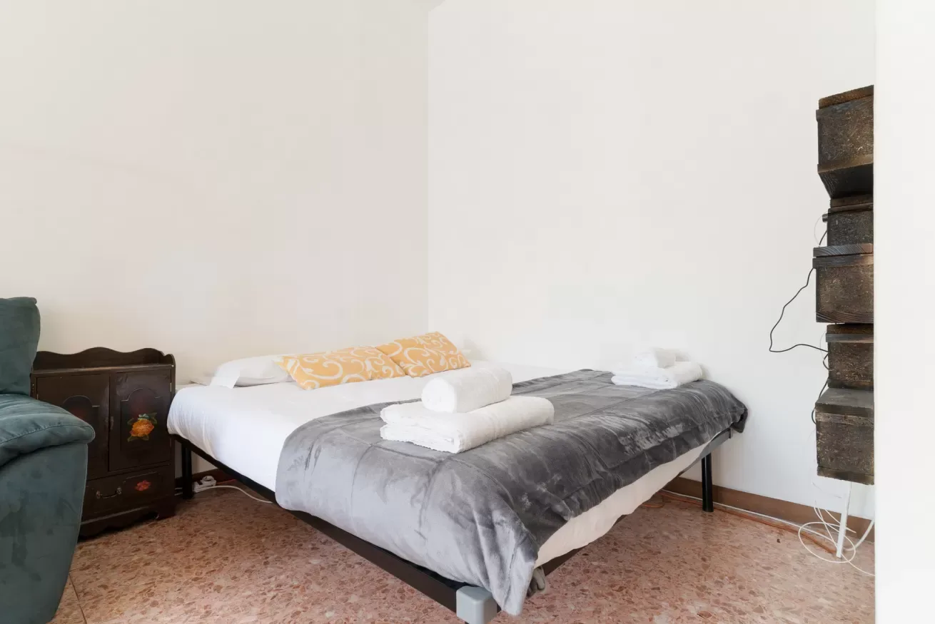 A bedroom with a bed covered in white linens and a gray blanket.