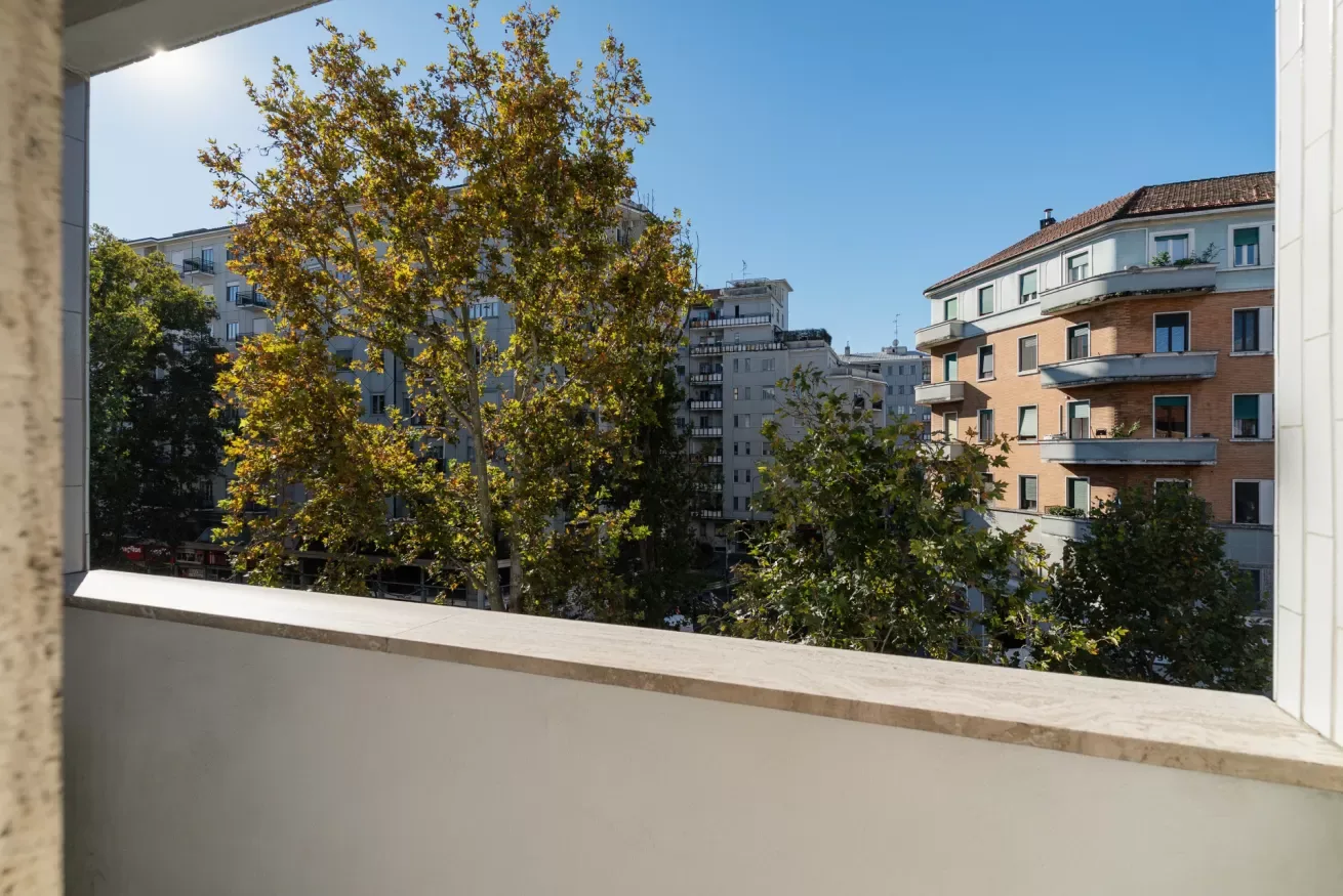 A city view through an open window, with trees and apartment buildings.