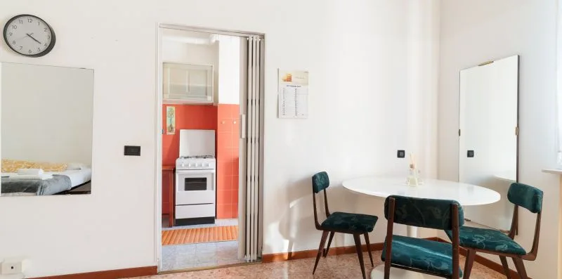 A dining area with a round table and green seating beside a kitchen doorway.