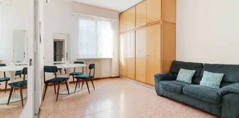 A bright living room with a dining table and dark seating beside wooden cabinets.