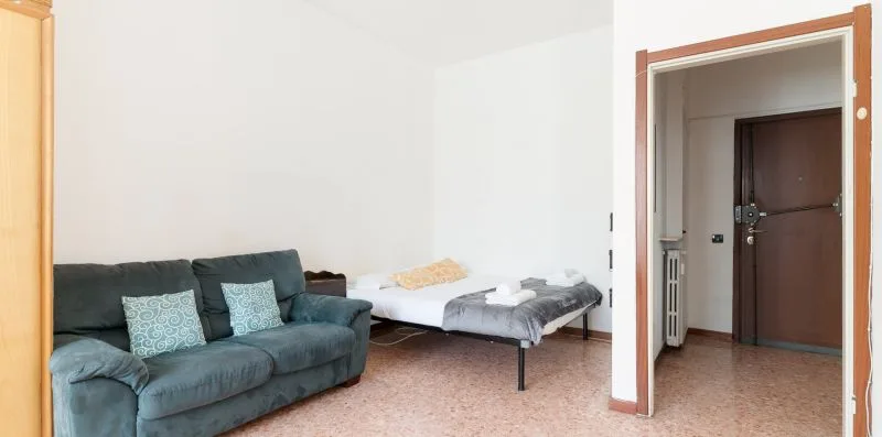 A living area with dark seating and a small bed beside an open doorway.