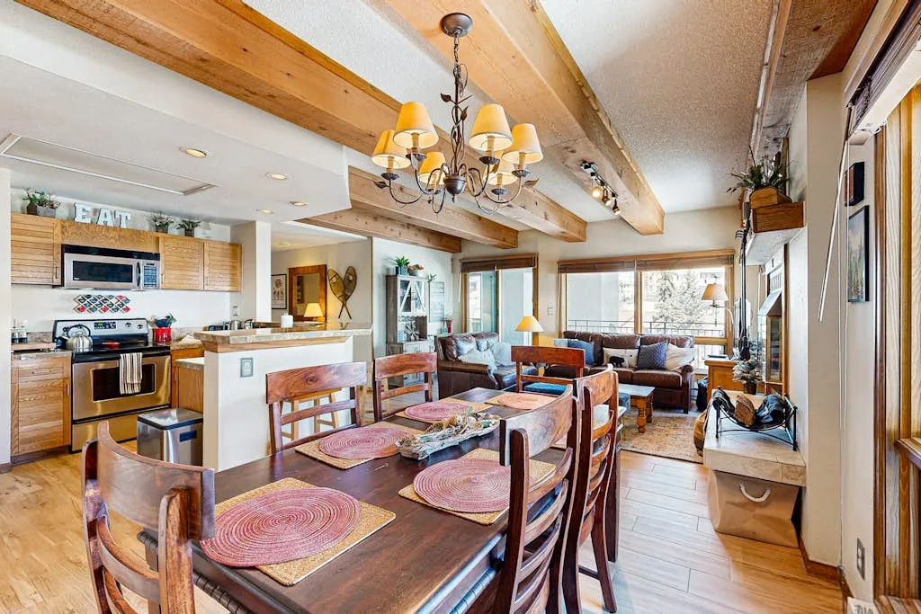 An open-plan dining and living area with a kitchen and wooden dining table.