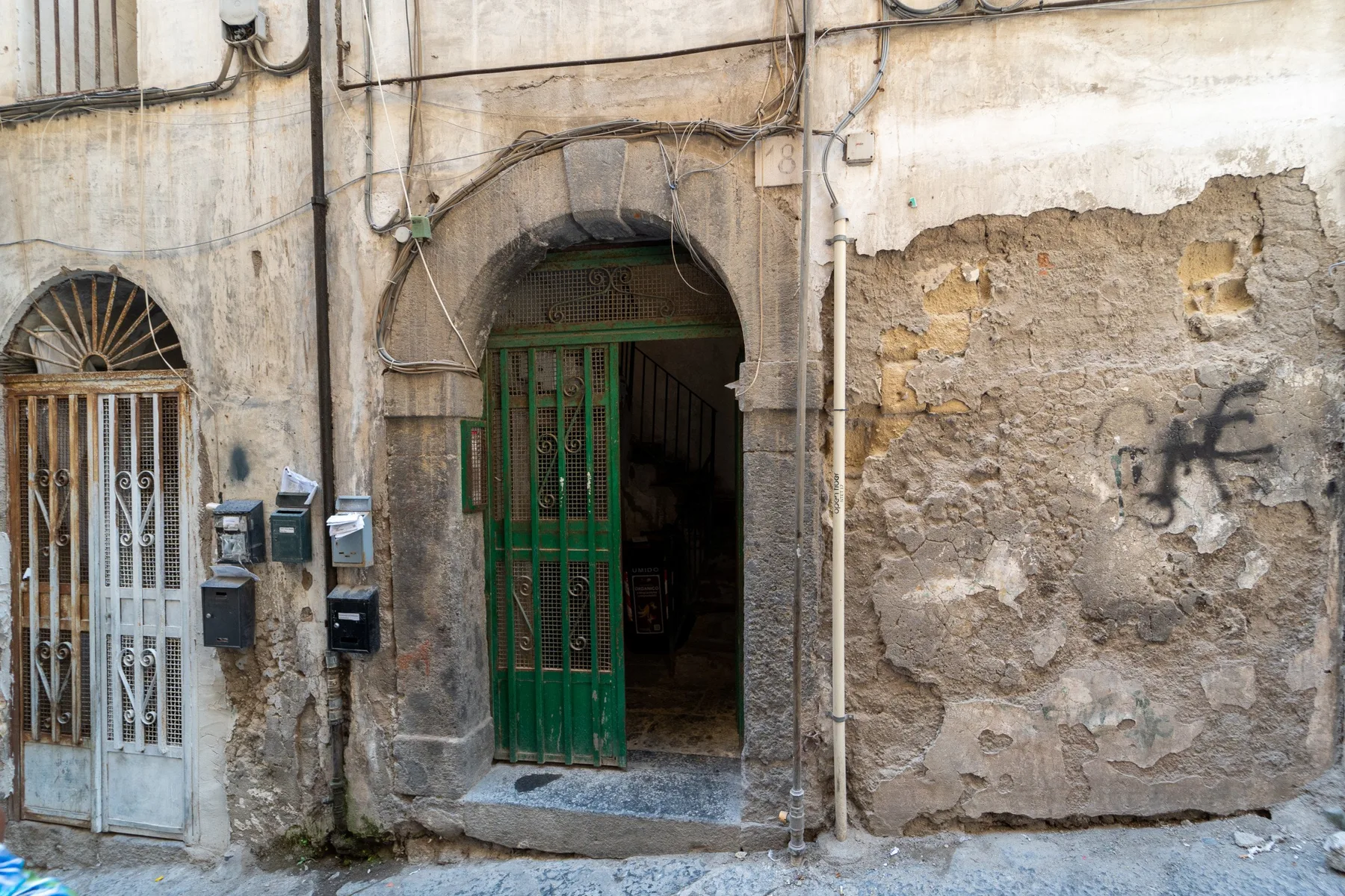 Fachada de un edificio antiguo de piedra con una reja verde en una entrada arqueada.