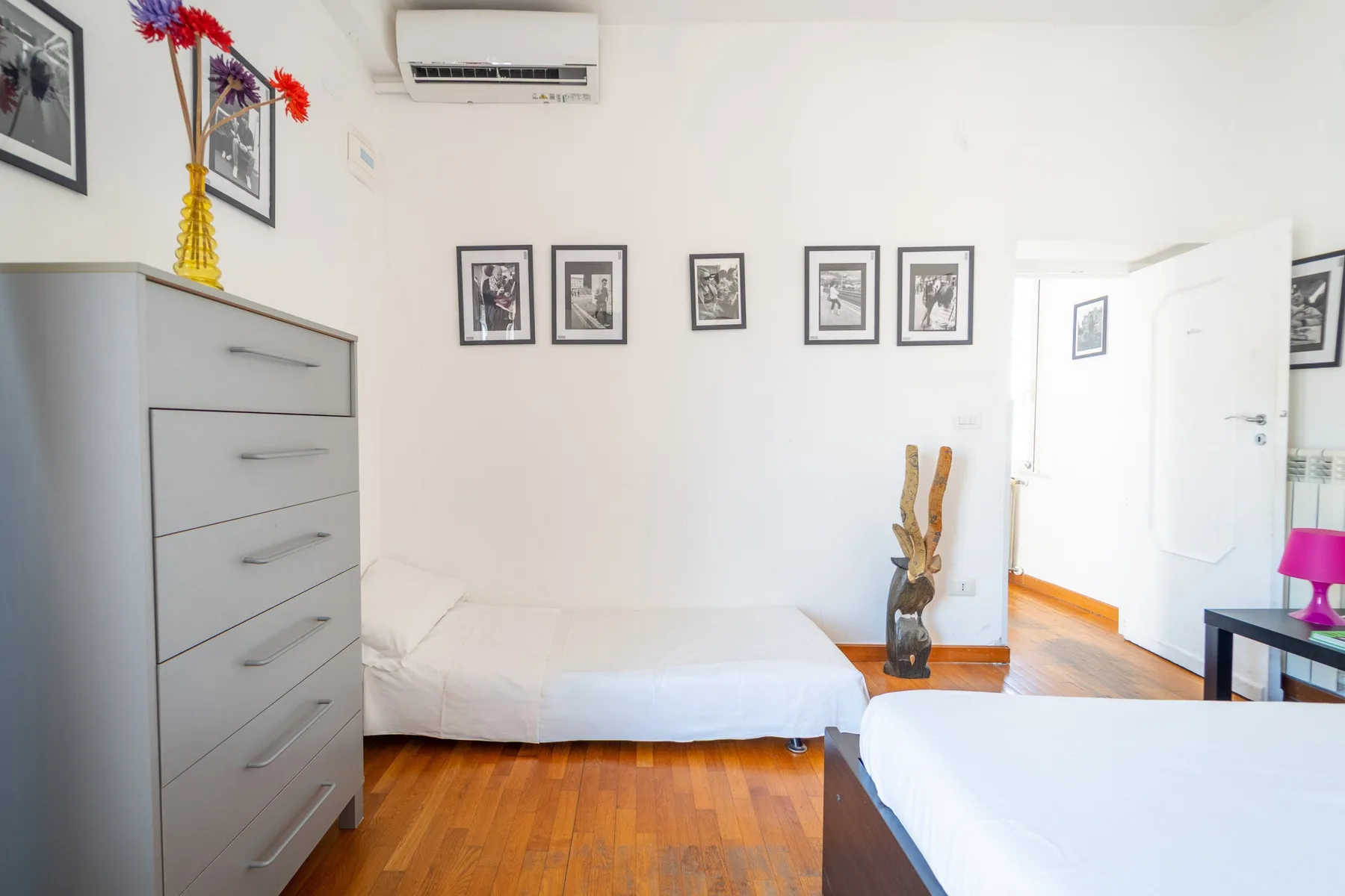Un dormitorio luminoso con camas blancas, cuadros enmarcados y suelo de madera.