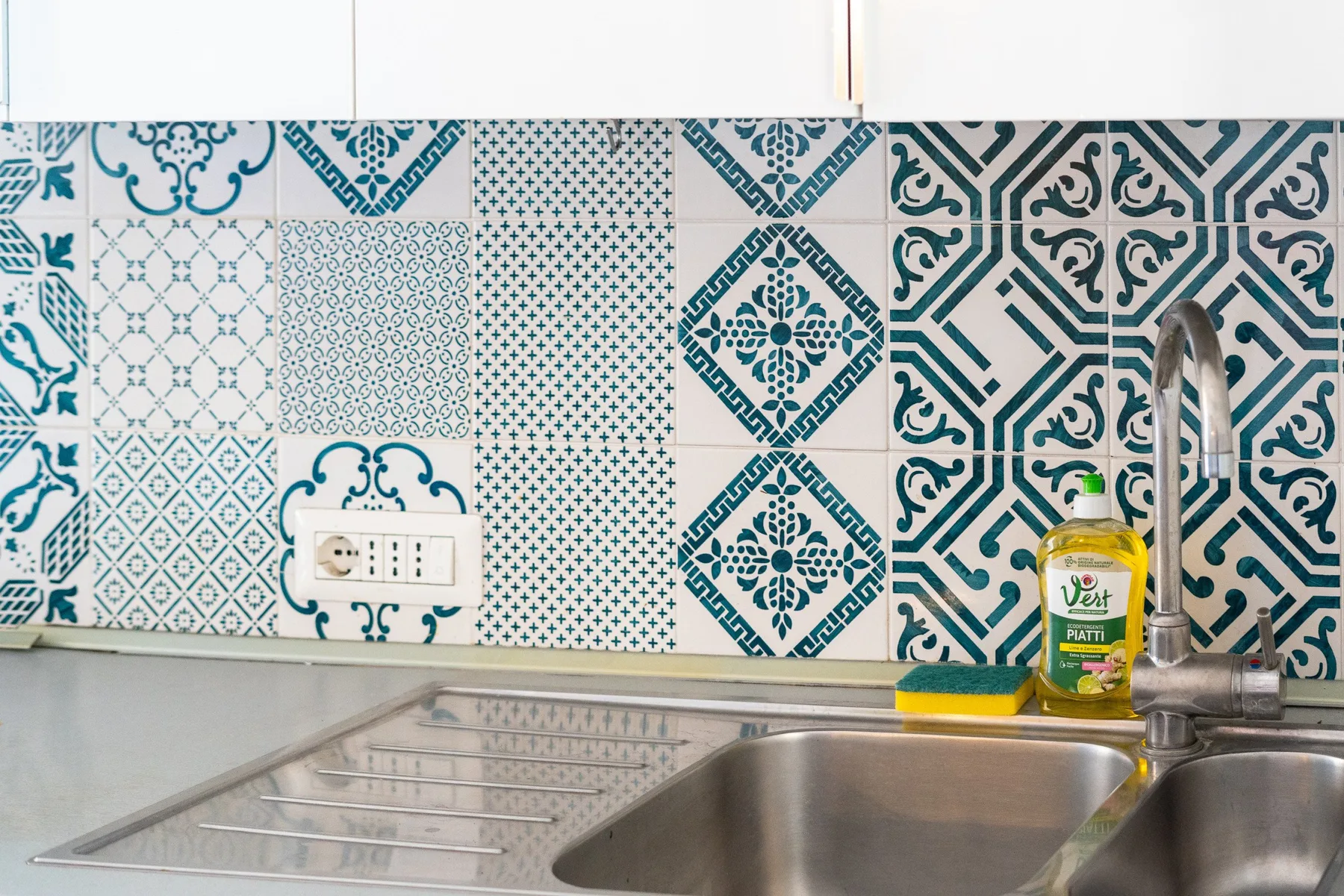 Un fregadero de cocina y un grifo están bajo una pared de azulejos estampados azules y blancos.