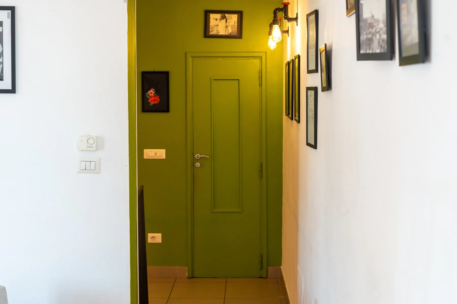 Un pasillo estrecho con una puerta verde y cuadros en las paredes.