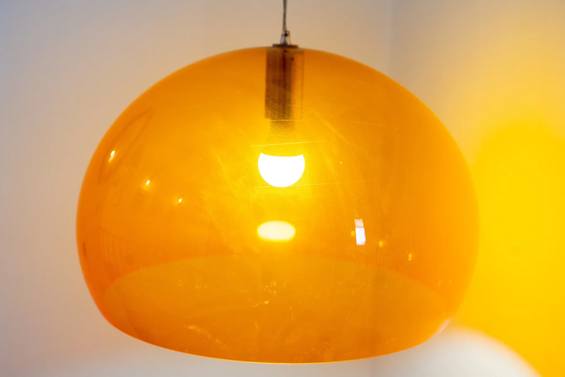 Primer plano de una lámpara colgante naranja encendida frente a una pared clara.