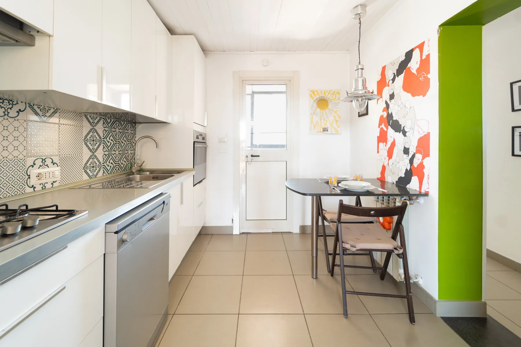 Una cocina luminosa con gabinetes blancos, un salpicadero de azulejos y una pequeña mesa de comedor.