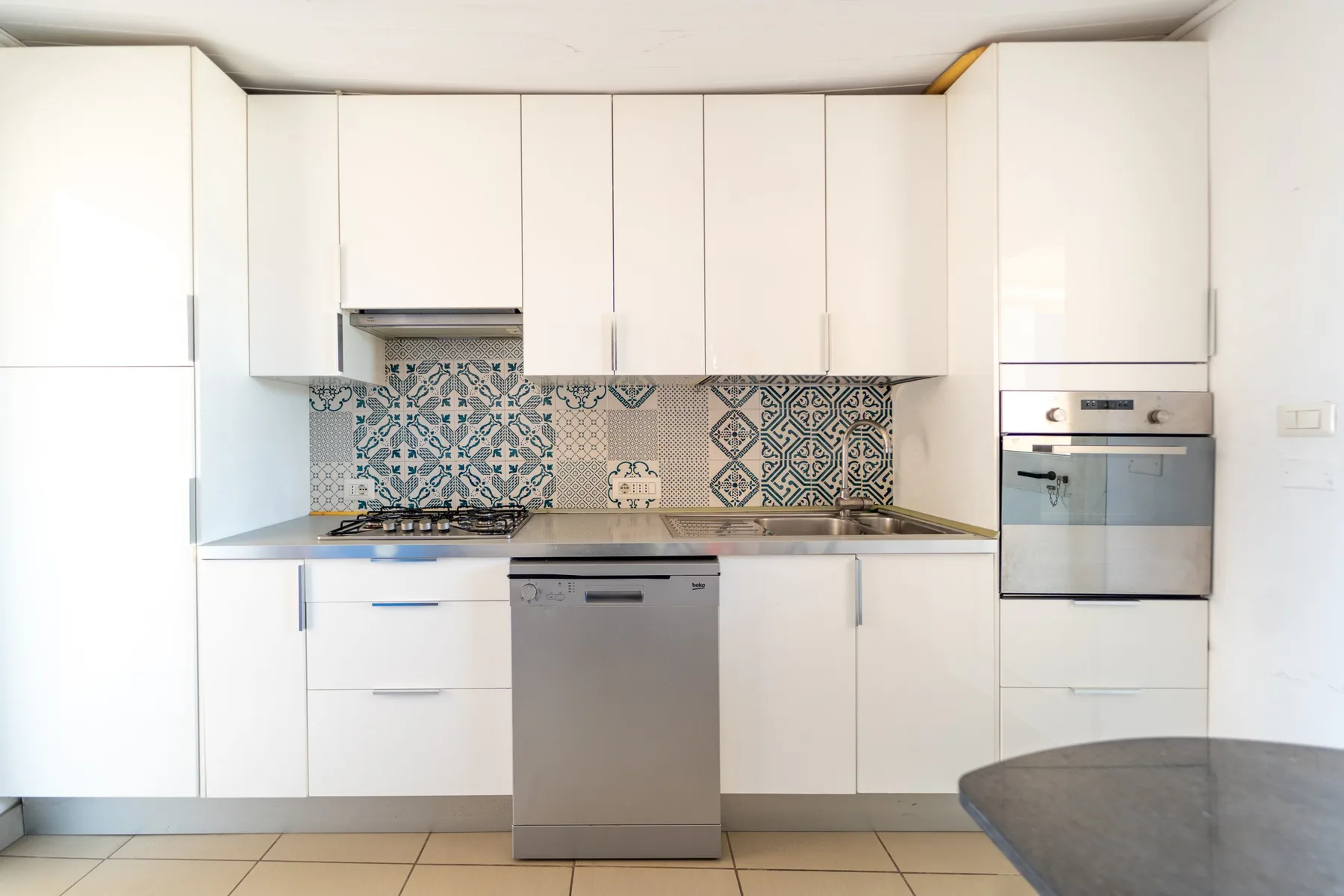 Una cocina moderna y luminosa con gabinetes blancos, un salpicadero estampado y electrodomésticos de acero inoxidable.