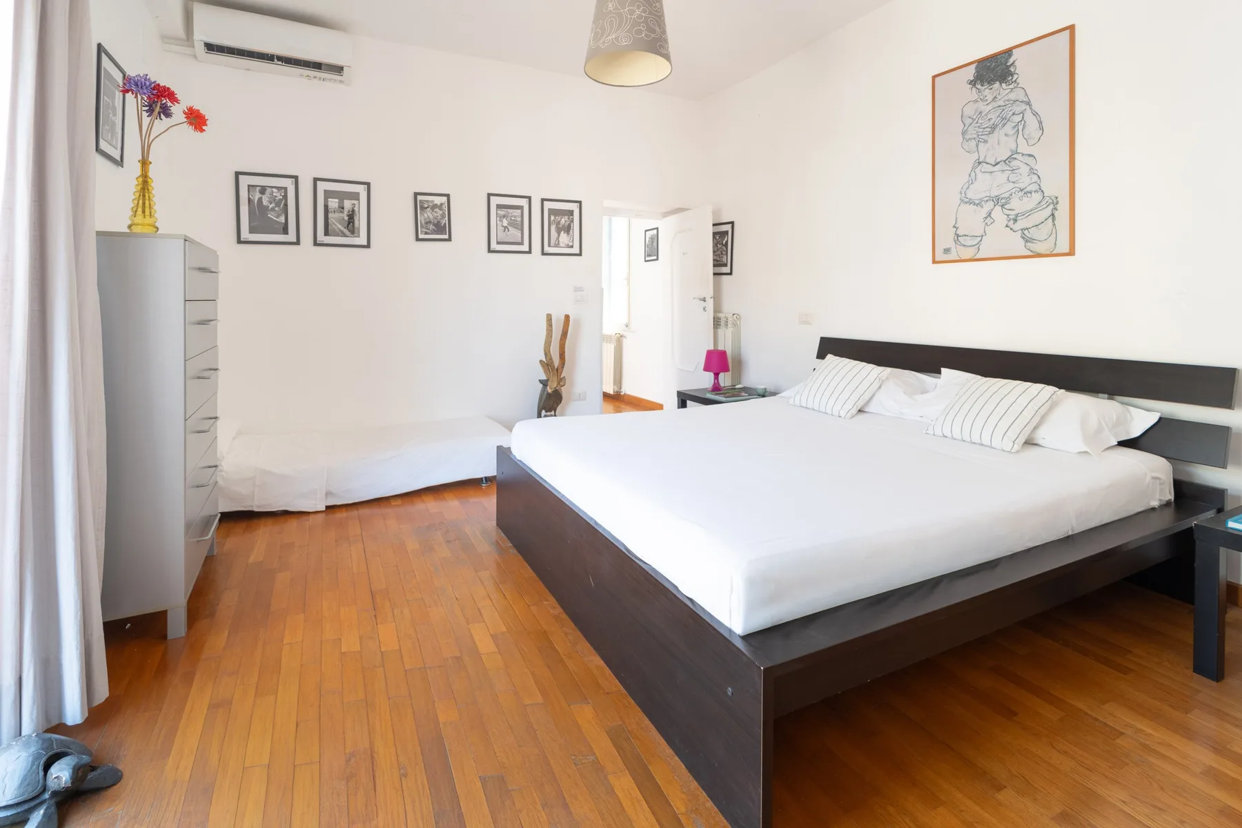 Un dormitorio luminoso con una cama grande, cuadros enmarcados y suelo de madera.
