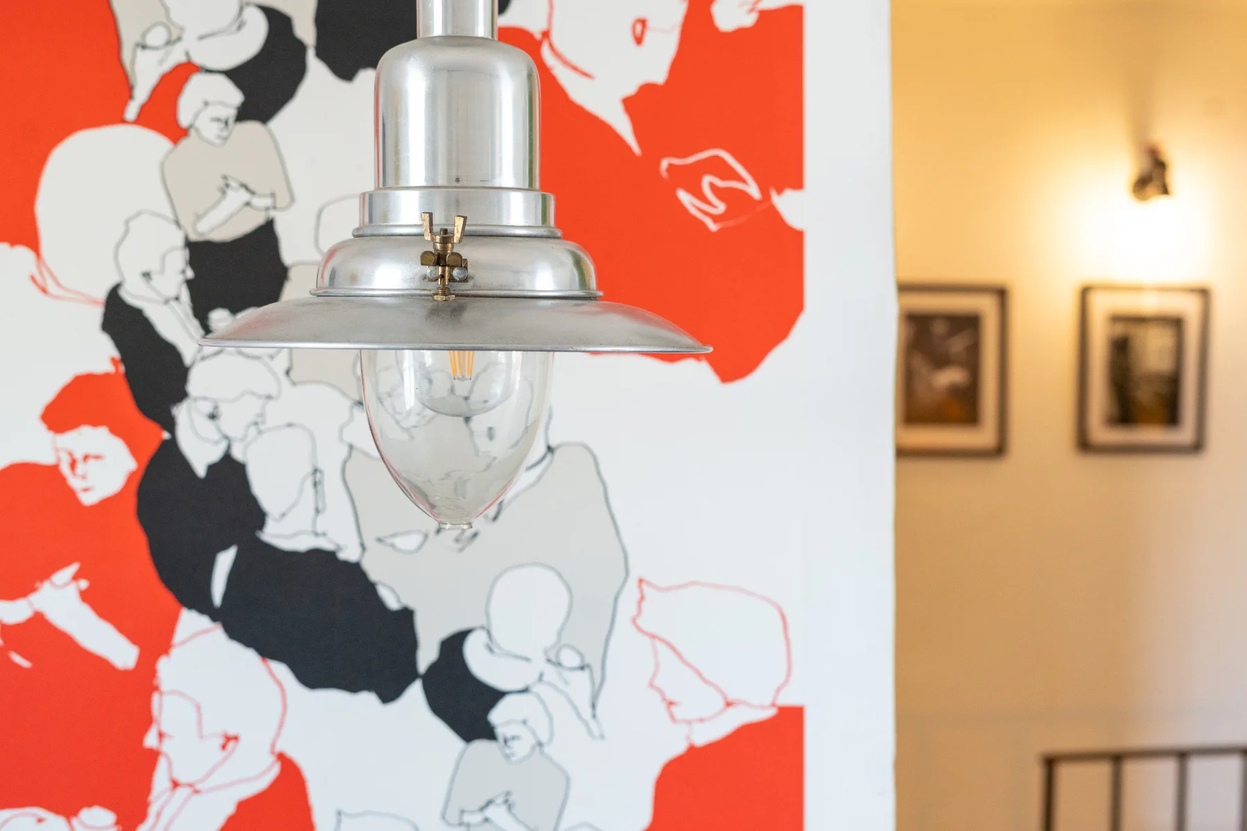 Una lámpara colgante está frente a una llamativa ilustración mural en rojo, negro y blanco.