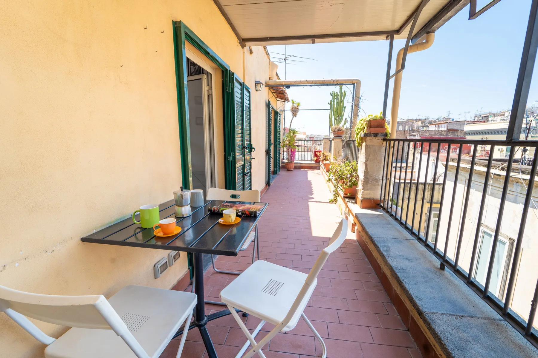 Una terraza cubierta con una mesa pequeña y asientos junto a una puerta abierta.