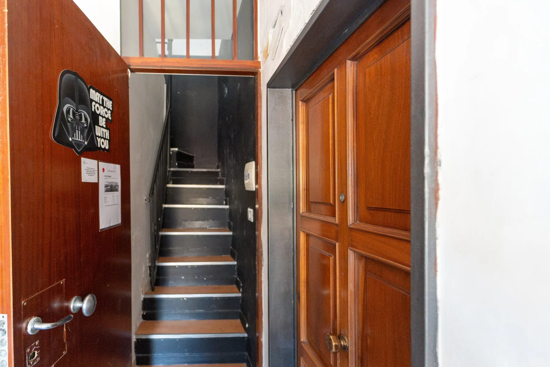 Una escalera interior con peldaños oscuros entre puertas de madera.