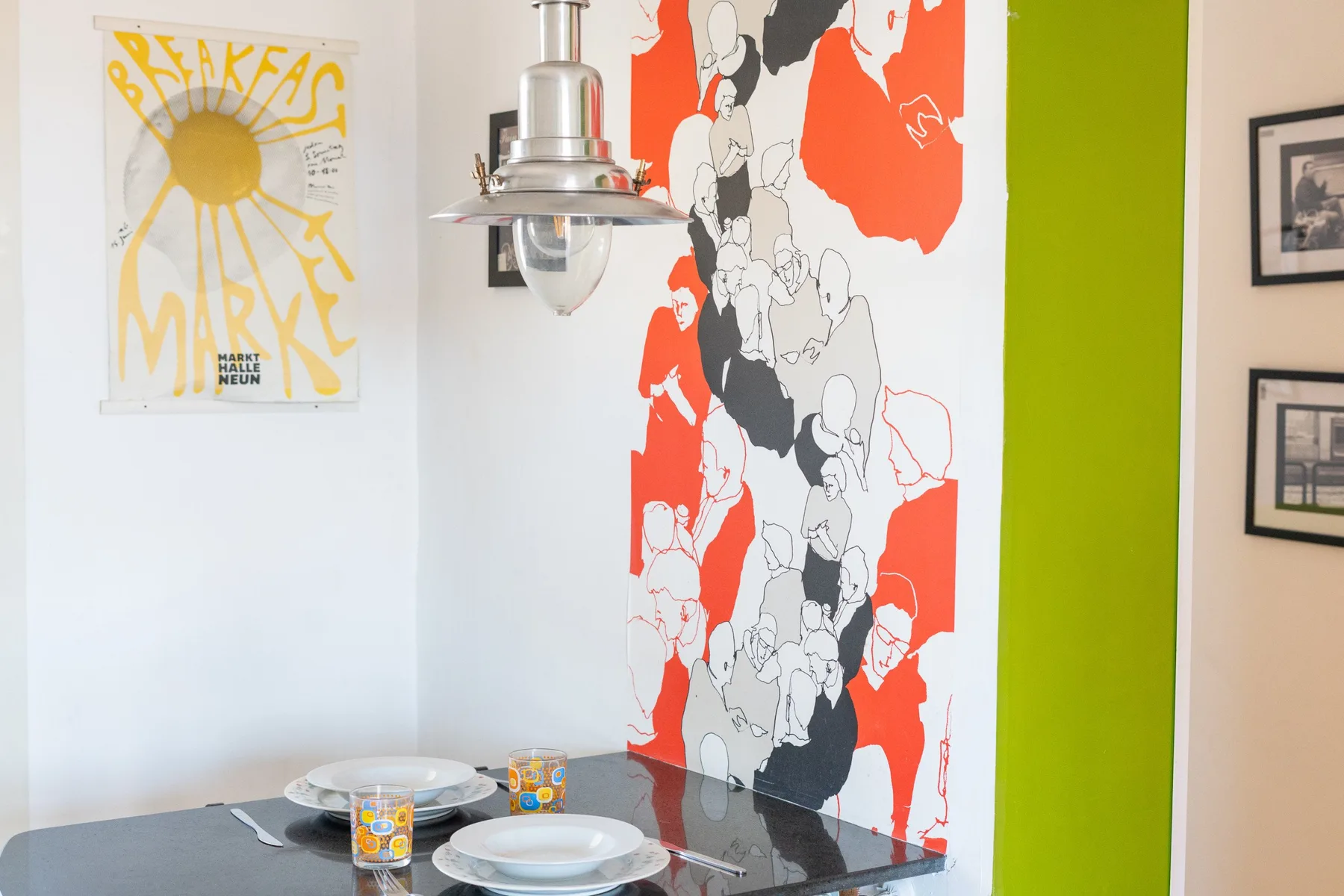 Una mesa de comedor está junto a un mural colorido y una pared verde brillante.