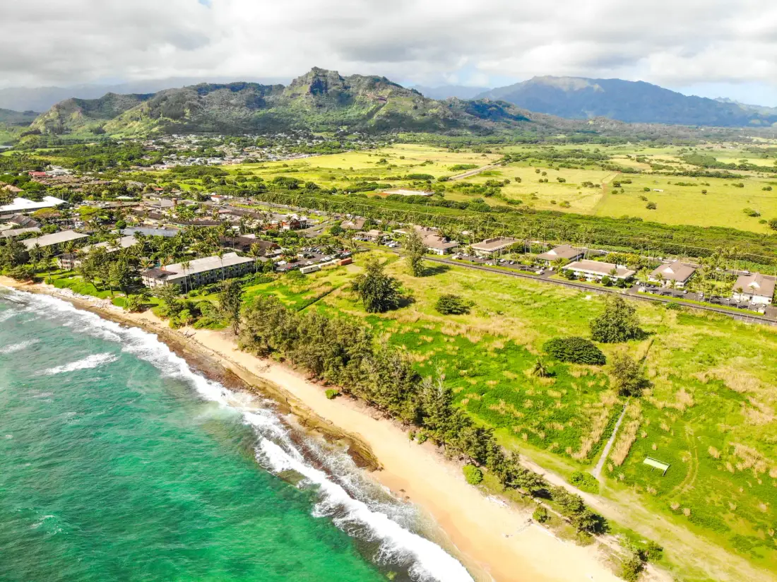 Aerial view of a tropical coastline with green fields and mountains inland.