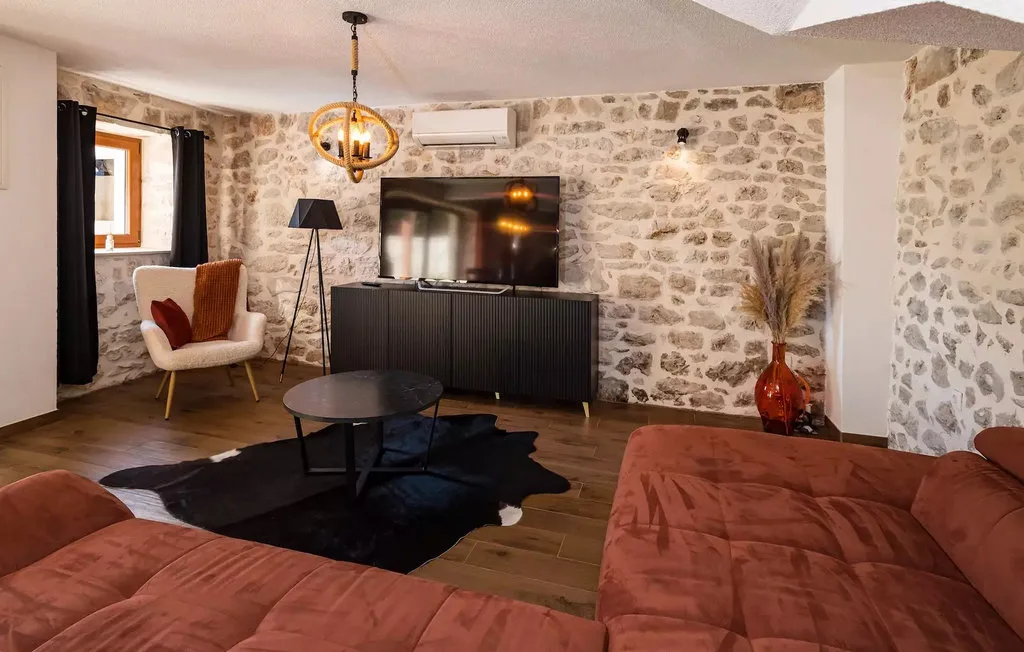 A living room with stone walls, rust-colored seating, and a television.