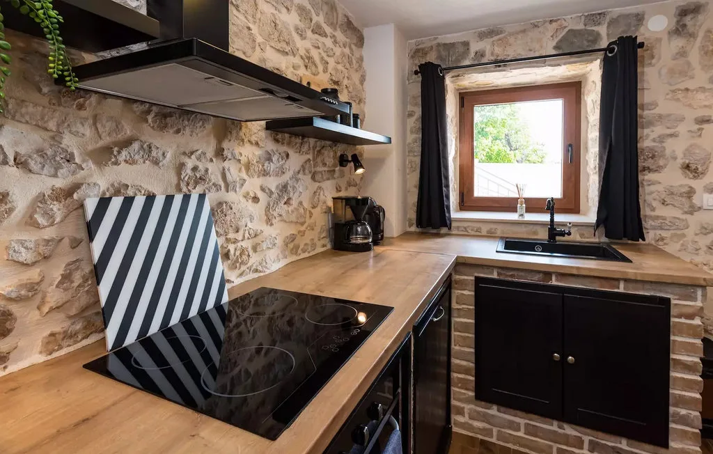 A rustic kitchen with stone walls, wooden counters, a cooktop, and a window above the sink.