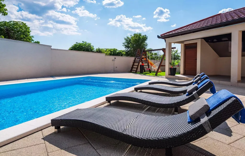 An outdoor swimming pool beside a paved patio with reclining loungers.