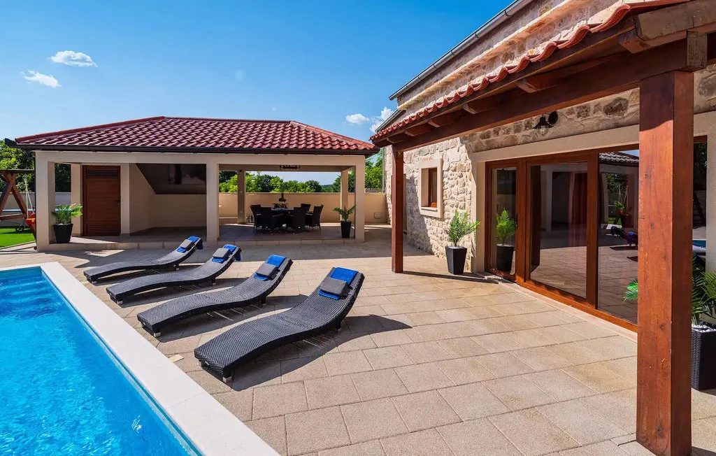 A sunny poolside patio with lounge seating and a covered outdoor dining area.