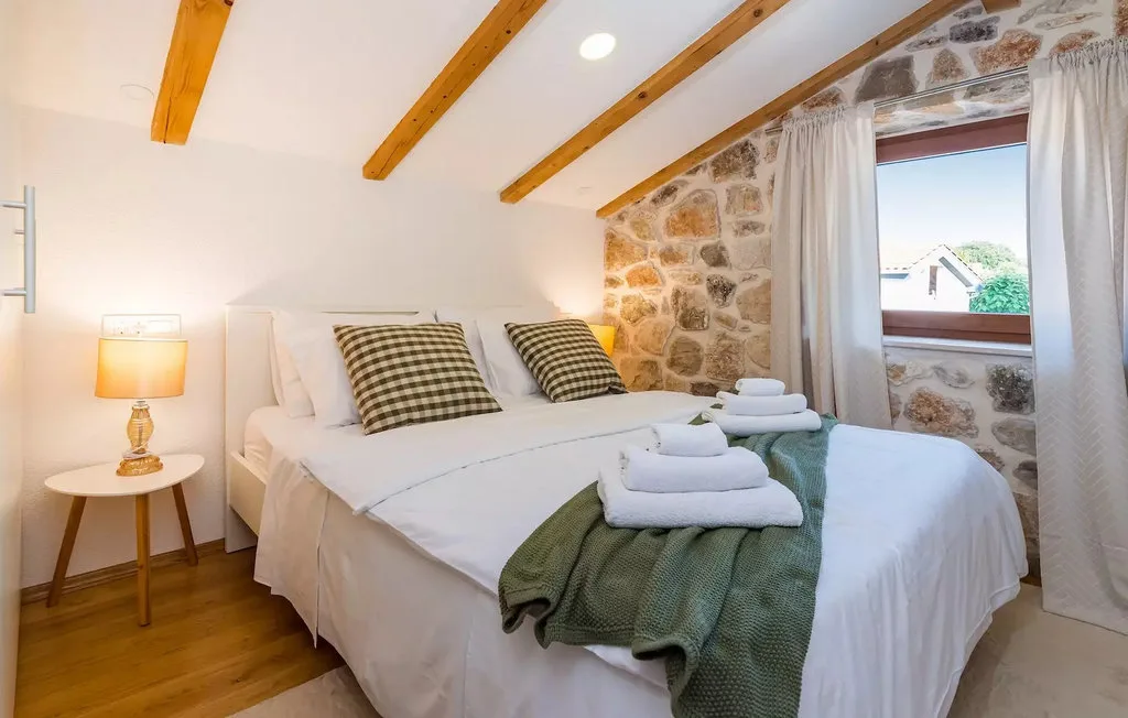 A bright bedroom with white bedding, folded towels, and a stone wall.