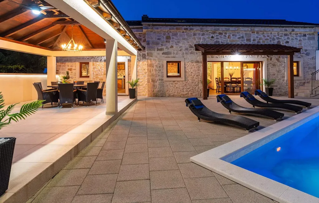 A paved patio beside a pool, with lounge seating and a covered dining area.