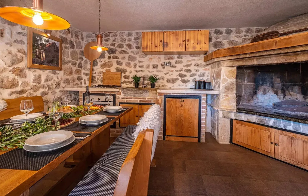 A rustic dining area with a long table beside a large stone fireplace.