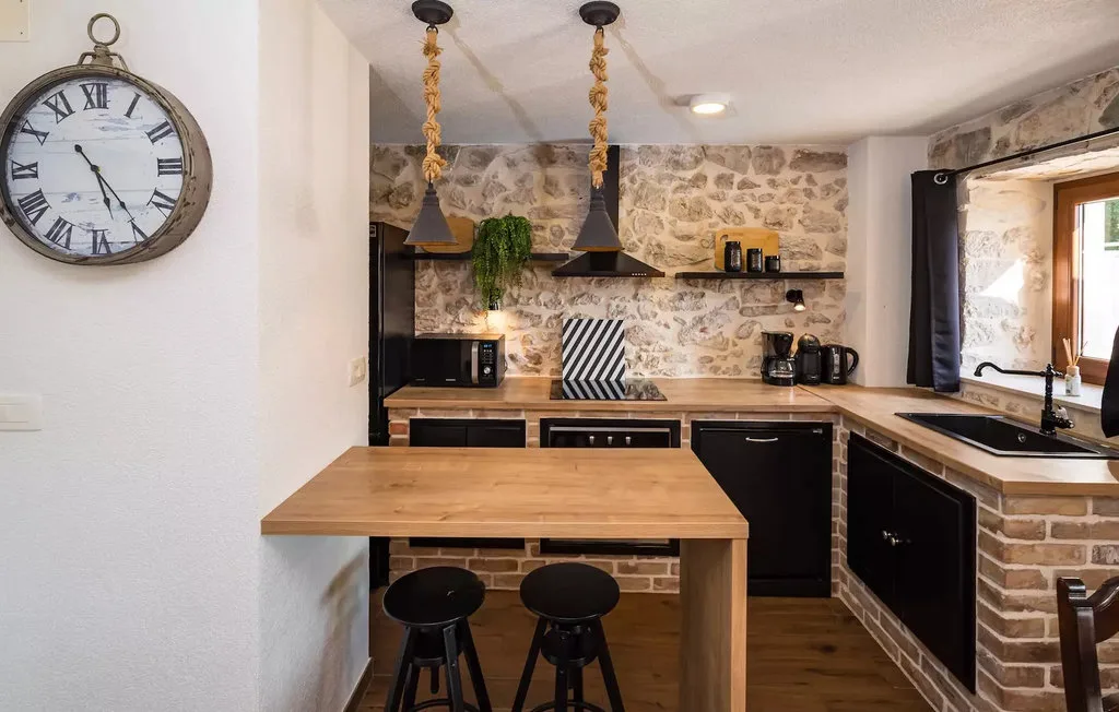 A kitchen with a wooden counter, dark cabinetry, and a stone-patterned backsplash.