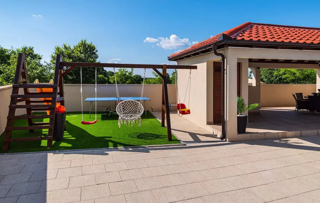 An outdoor patio with a pergola, swings, and a paved seating area.