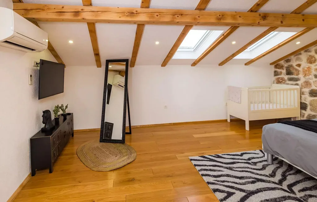 A bedroom with a wooden floor, exposed ceiling beams, and a bed.