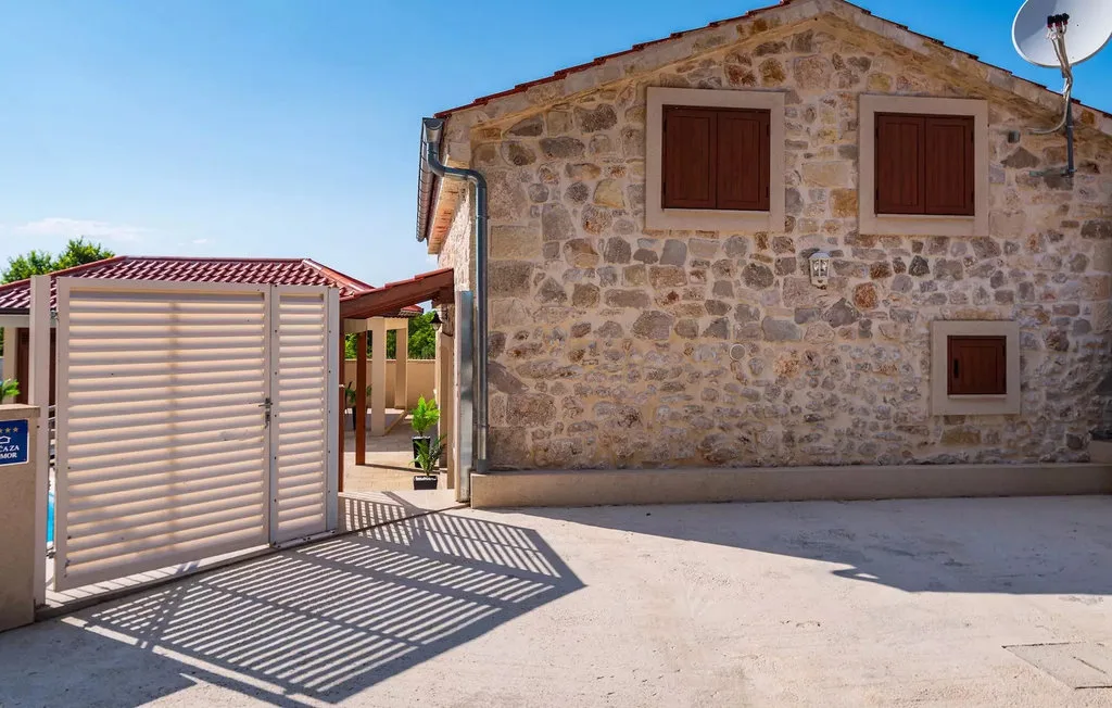 A stone building with closed wooden shutters beside a slatted gate.