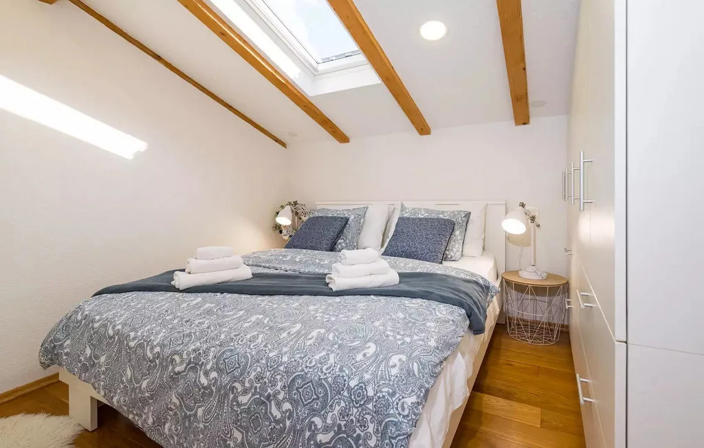 A bedroom with a bed beneath exposed wooden ceiling beams and a skylight.