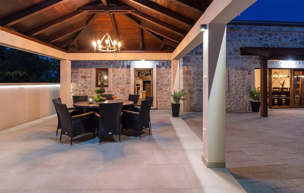 Covered stone patio with a dining table and seating beneath a timber roof.