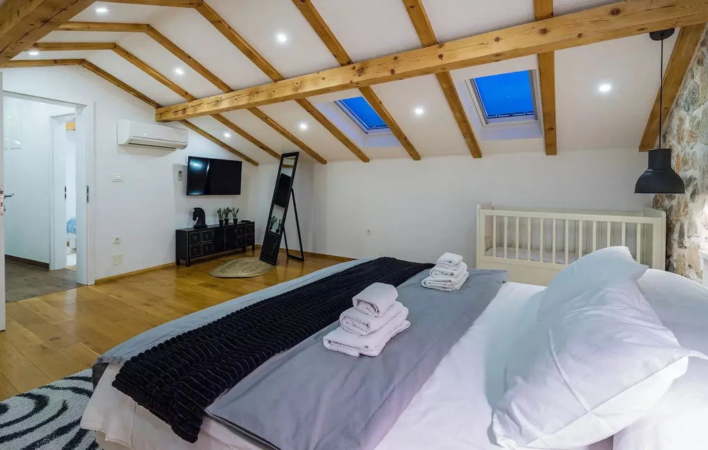 A bedroom with a low bed beneath exposed wooden ceiling beams.