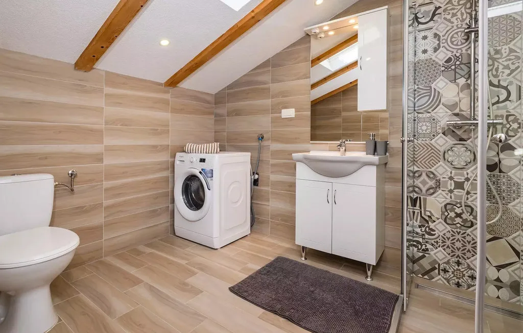 A tiled bathroom with a vanity, washing machine, and glass shower.