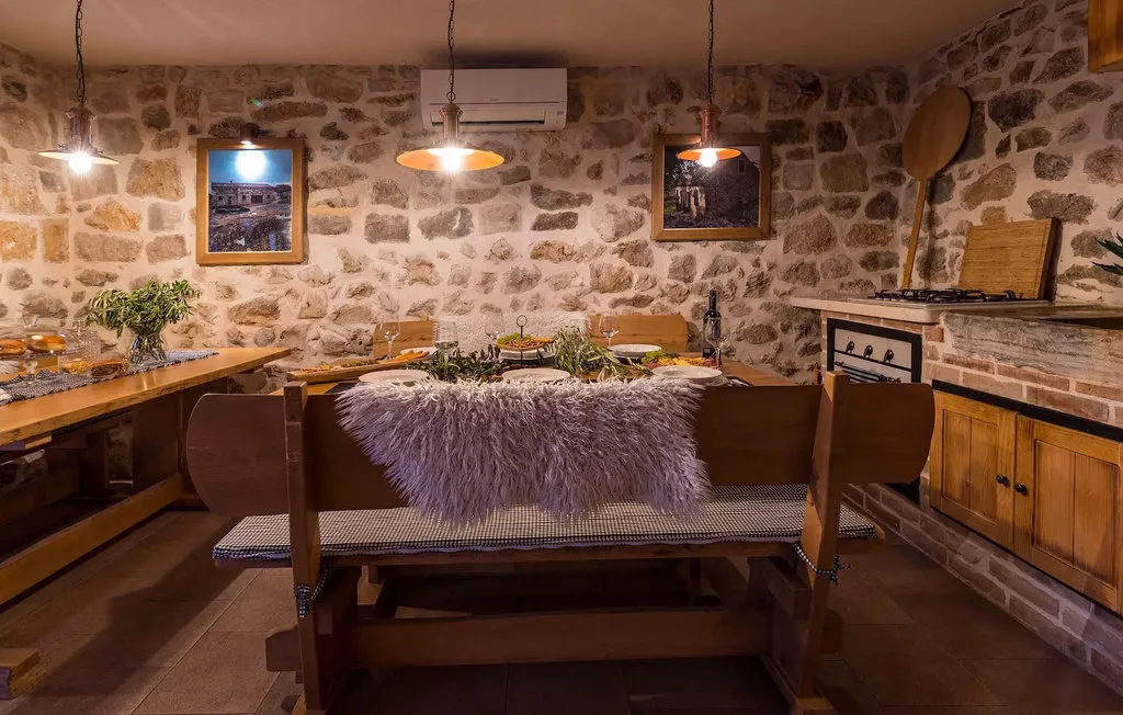 A rustic dining room with a long table, wooden seating, and stone walls.