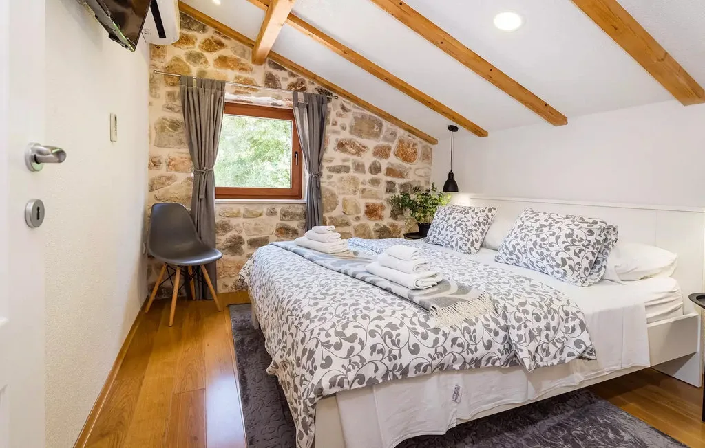 A bedroom with a double bed, patterned bedding, and a window set in a stone wall.
