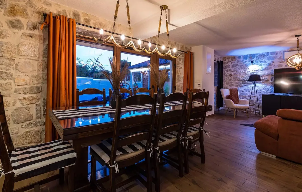 A dining area with a long table beside large windows overlooking a pool.