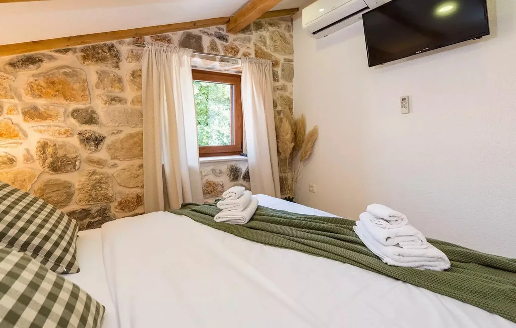 A bedroom with a bed, folded towels, and a window set in a stone wall.