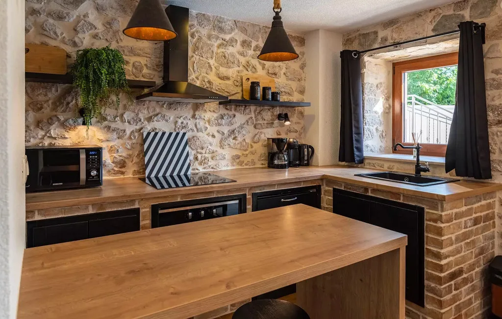 A rustic kitchen with stone walls, dark cabinets, and a wooden island.