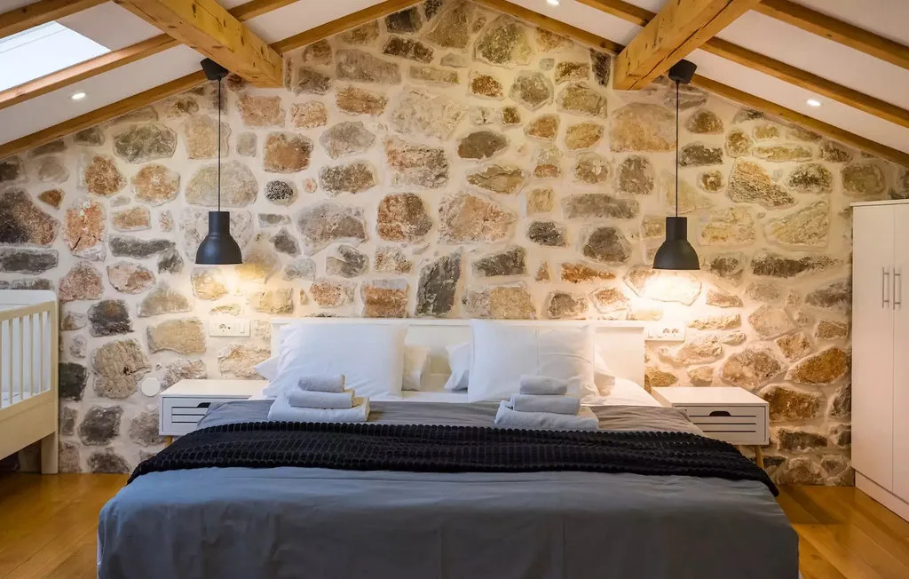 A bedroom with a bed beneath exposed wooden beams and pendant lights.