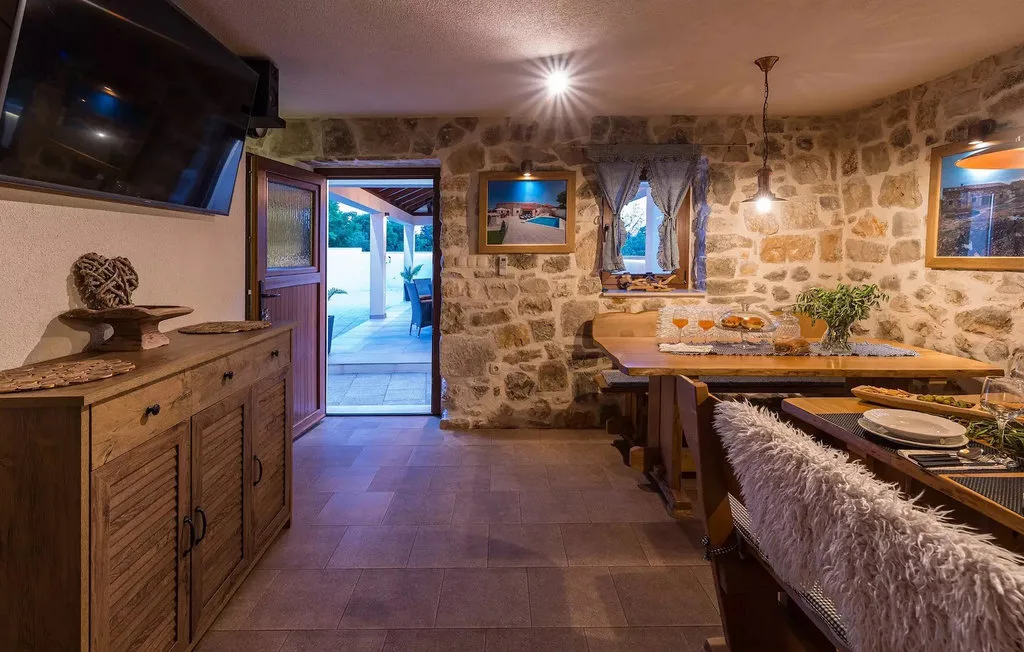A stone-walled dining area with a long table and a doorway opening to the outside.