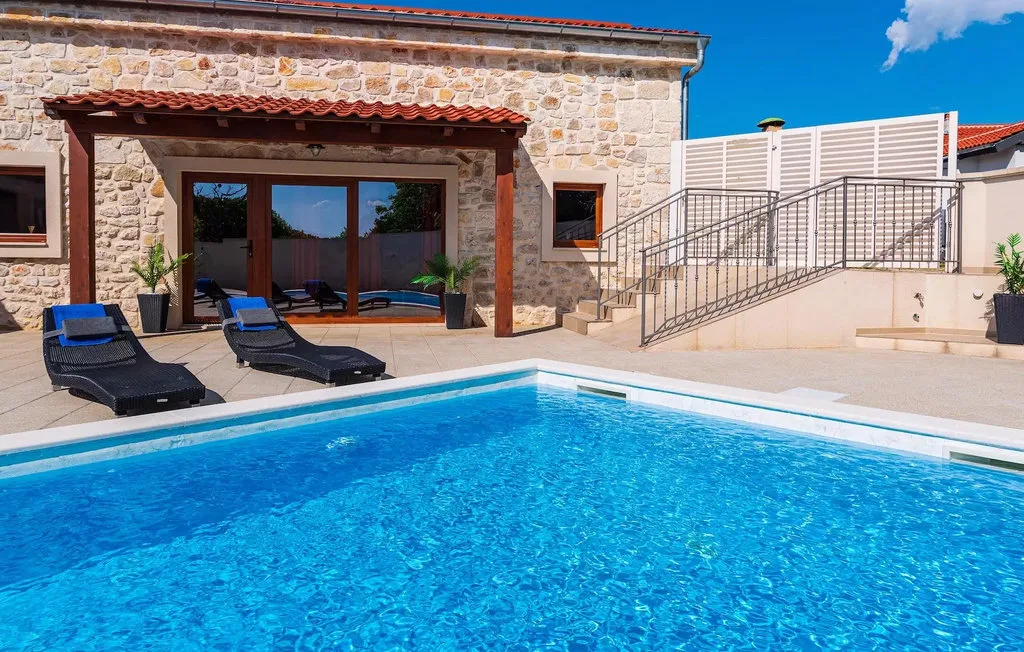 A swimming pool beside a stone house and outdoor seating.