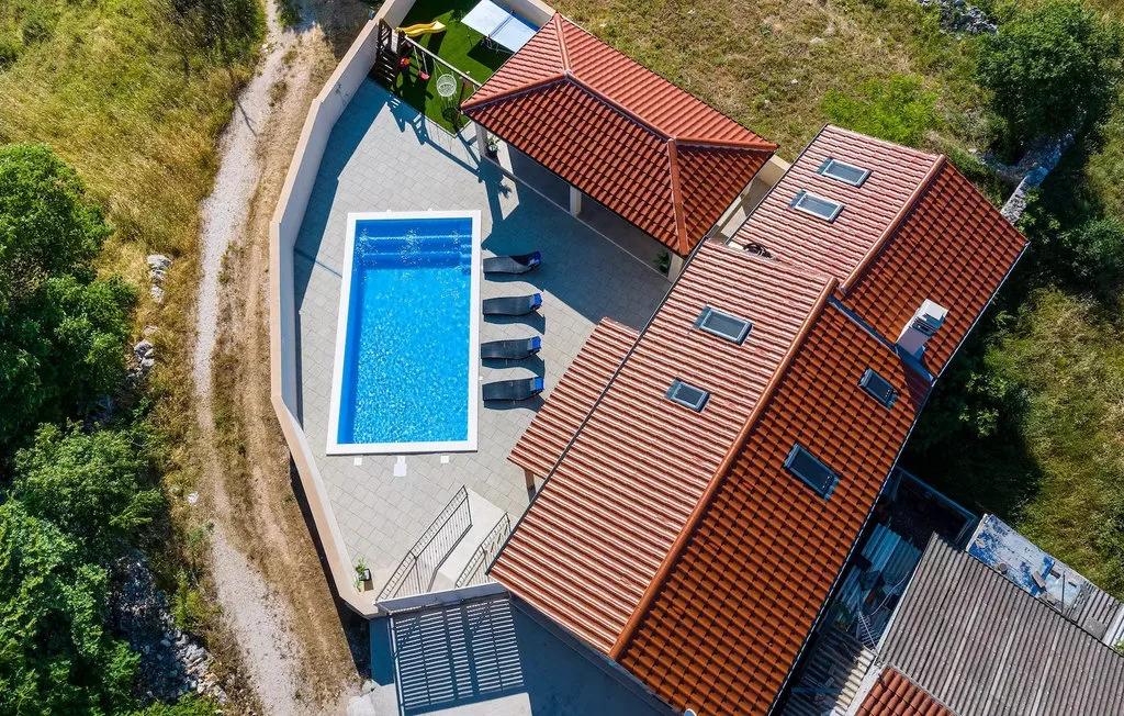 An aerial view shows a red-tiled building beside a swimming pool.
