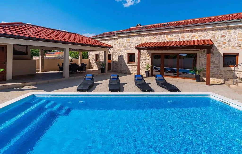 An outdoor swimming pool sits beside a stone building and shaded patio.