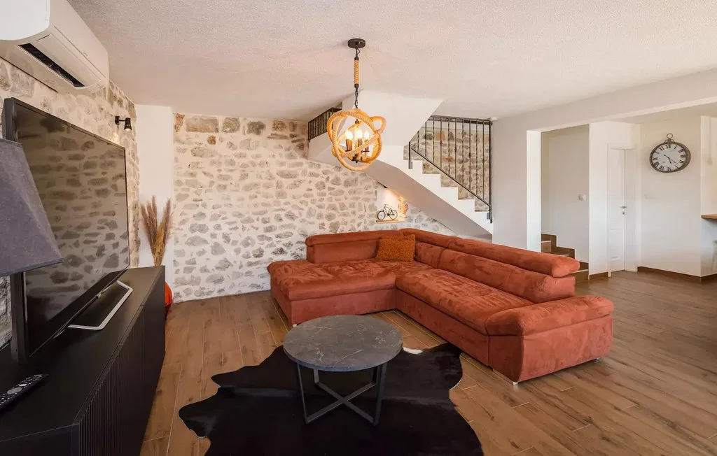 A living room with an orange sectional, a coffee table, and a stone wall.