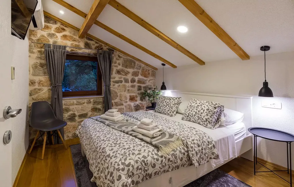 A bedroom with patterned bedding and exposed wooden ceiling beams.