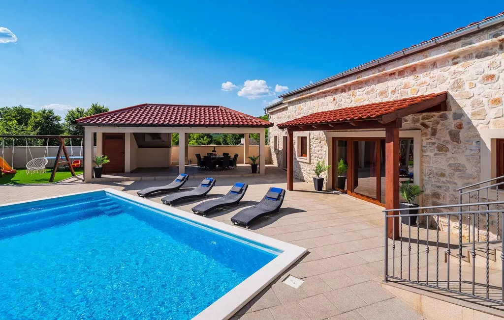 A swimming pool beside a stone house and covered outdoor seating area.