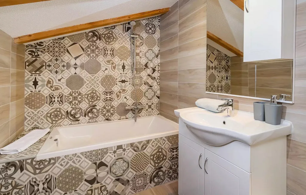 A bathroom with a bathtub, patterned tile, and a sink.